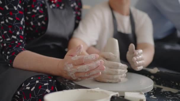 Un maestro donna condivide le sue abilità dando una lezione per gli anziani. Mostra alla nonna la tecnica di lavorare su una ruota di vasai con argilla ceramica — Video Stock