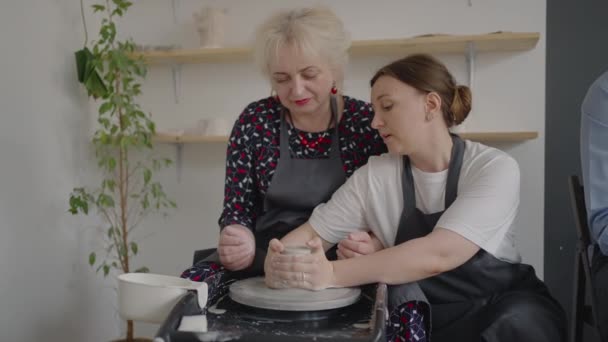 Une maitrise partage ses compétences tout en donnant une leçon aux personnes âgées. Montrer à grand-mère la technique de travail sur une roue de potiers avec de l'argile céramique — Video