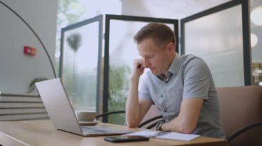 Güzel bir erkek müteahhit ya da öğrenci kafede dizüstü bilgisayarla çalışıyor. Serbest meslek, uzaktan eğitim, online eğitim, serbest meslek