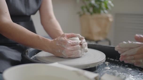 Uma professora de escultura de rodas de oleiros explica como trabalhar e ensina uma mulher idosa a trabalhar com barro e fazer canecas e jarros. Master class para pensionistas. Cursos de cerâmica — Vídeo de Stock