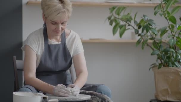 Oudere vrouw ambachtsman werken aan een pottenbakkerswiel voor het maken van klei en keramische kannen en borden in slow motion — Stockvideo