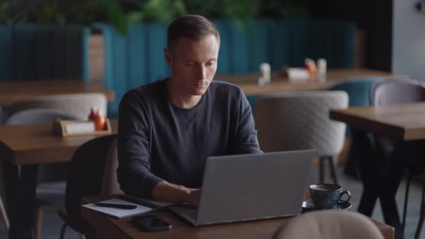 Hermoso desarrollador masculino o estudiante trabajando, estudiando por computadora portátil en la cafetería. cuentapropistas, trabajo a distancia, educación en línea, autoempleo — Vídeo de stock