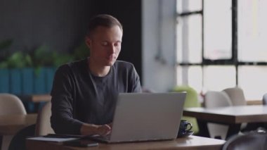 Güzel bir erkek müteahhit ya da öğrenci kafede dizüstü bilgisayarla çalışıyor. Serbest meslek, uzaktan eğitim, online eğitim, serbest meslek