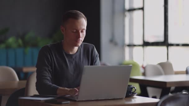 Hermoso desarrollador masculino o estudiante trabajando, estudiando por computadora portátil en la cafetería. cuentapropistas, trabajo a distancia, educación en línea, autoempleo — Vídeos de Stock