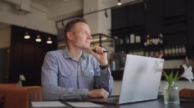 Düşünceli, ciddi, genç bir öğrenci yazar dizüstü bilgisayarla oturup düşüncelere dalmış, düşüncelere dalmış, düşüncelere dalmış hayaller kuruyor.