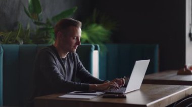 Güzel bir erkek müteahhit ya da öğrenci kafede dizüstü bilgisayarla çalışıyor. Serbest meslek, uzaktan eğitim, online eğitim, serbest meslek