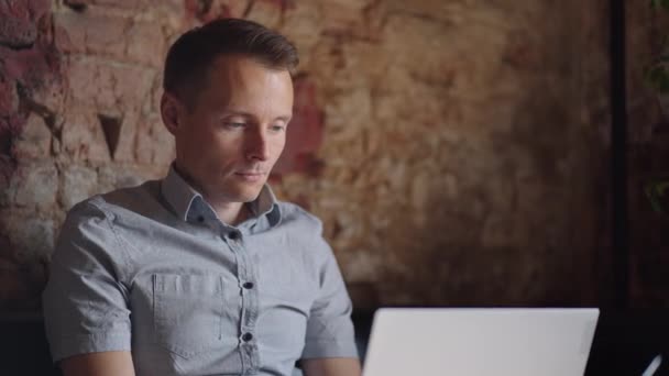 Um homem sério é um estudante de negócios que trabalha estudando sentado em uma mesa e digitando uma mensagem em um laptop. Escrevendo texto no teclado — Vídeo de Stock