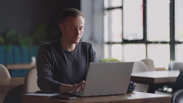 Um homem sério é um estudante de negócios que trabalha estudando sentado em uma mesa e digitando uma mensagem em um laptop. Escrevendo texto no teclado — Vídeo de Stock