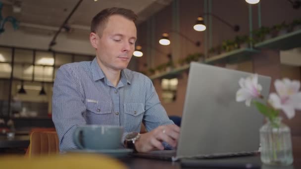 Un hombre serio es un estudiante de negocios que trabaja estudiando sentado en una mesa y escribiendo un mensaje en una computadora portátil. Escribir texto en el teclado — Vídeo de stock