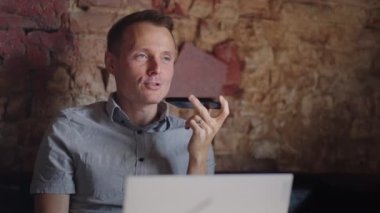 Gülümseyen genç adam hoparlörden ses tanıma mesajı kaydediyor. İş adamı sanal asistan uygulaması kullanıyor. Dahili ofisteki akıllı telefondan anımsatıyor. Dijital ai mobil yardım teknolojisi kavramı