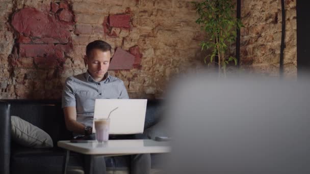 Um homem sério é um estudante de negócios que trabalha estudando sentado em uma mesa e digitando uma mensagem em um laptop. Escrevendo texto no teclado — Vídeo de Stock