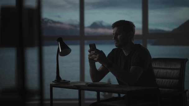 Silhuett av en man som sitter vid ett bord och tittar på en mobiltelefon tänkande och analysera aktiemarknaden, lösa personliga problem, återbetalning av lån, Internetbank — Stockvideo