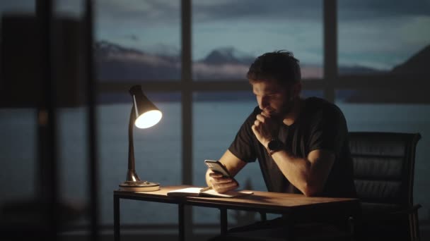 Silhouette eines Mannes, der an einem Tisch sitzt und ein Mobiltelefon betrachtet, das den Aktienmarkt analysiert, persönliche Probleme löst, Kredite zurückzahlt, Internet-Banking — Stockvideo