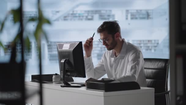 Um homem sério senta-se num computador no escritório e pensa. Analisa resolve um problema de crise. Uma fase difícil no negócio. Empresário atencioso — Vídeo de Stock