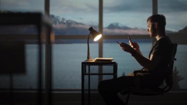 Masada oturan bir adamın silueti cep telefonuna bakıyor ve borsayı inceliyor, kişisel sorunları çözüyor, kredilerin geri ödenmesi, internet bankacılığı...