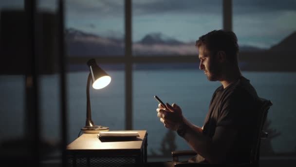 Silhouette d'un homme assis à une table regardant un téléphone portable penser et analyser le marché boursier, résoudre des problèmes personnels, remboursement de prêts, services bancaires sur Internet — Video