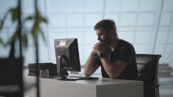 Um homem sério senta-se num computador no escritório e pensa. Analisa resolve um problema de crise. Uma fase difícil no negócio. Empresário atencioso — Vídeo de Stock