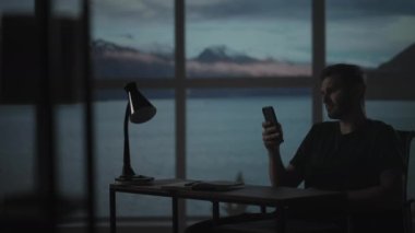 Masada oturan bir adamın silueti cep telefonuna bakıyor ve borsayı inceliyor, kişisel sorunları çözüyor, kredilerin geri ödenmesi, internet bankacılığı...