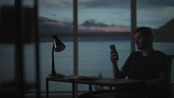 Silhouette di un uomo seduto a un tavolo a guardare un telefono cellulare che pensa e analizza il mercato azionario, risolve problemi personali, rimborsa prestiti, Internet banking — Video Stock