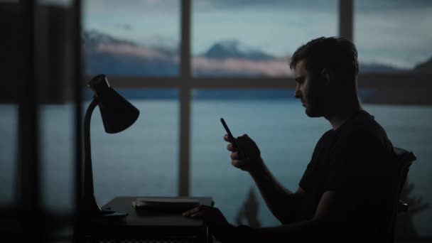 Σιλουέτα ενός ανθρώπου που κάθεται σε ένα τραπέζι κοιτάζοντας ένα κινητό τηλέφωνο σκέψης και ανάλυσης του χρηματιστηρίου, επίλυση προσωπικών προβλημάτων, αποπληρωμή των δανείων, Internet banking — Αρχείο Βίντεο