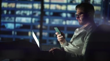 Ofis Binası İş Adamı Cep Telefonu Kullanıyor ve Ofis Penceresinin Yanında Bekliyor. Adam gece geç saatlerde modern ofiste çalışıyor. İşte cep telefonuyla meşgul Kafkas yöneticisi..