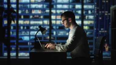 Odaklanmış iş adamı laptopta çalışıyor. Geceleri ofis masasında oturup notlar alıyor. Karanlık oda şehri ve genç yetişkin erkek profesyonel yönetici pazarlama araştırması yapıyor. 