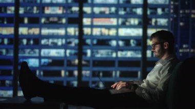 Odaklanmış, genç adam gece geç saatlere kadar dizüstü bilgisayarı üzerinde çalışırken kanepede uzanıyor. Yetişkin bir erkek gece evde, oturma odasında çalışıyor.