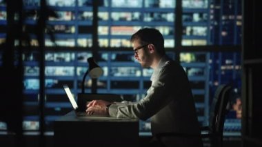 Geç saatlere kadar ofiste dizüstü bilgisayar başında çalışan yorgun bir genç adam. Uykucu iş adamı karanlık ofiste masa başında oturuyor. Gözlüklü, yorgun ve stresli iş adamı, şehir merkezinin bilgisayarında çalışıyor.
