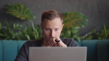 30 'lu yaşlardaki düşünceli bir adam sorun çözümünü dizüstü bilgisayarla düşünüyor. Piyasa risklerini göz önünde bulundurarak masa başında oturarak zor kararlar veren ciddi şüpheli bir erkek profesyonel.