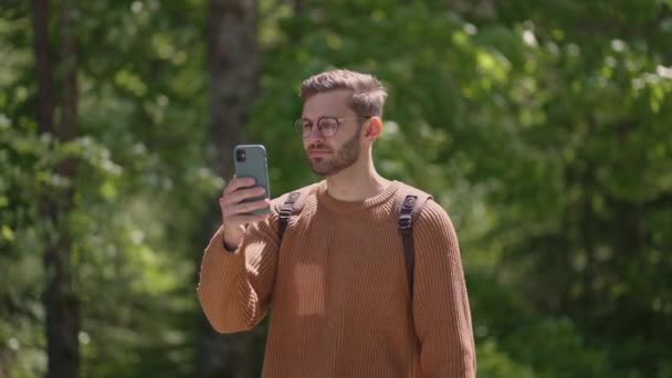 A young man with a backpack with a mobile phone walks in a forest area takes videos, photographs natural views. Creation of video content, online broadcast. — Stock Video