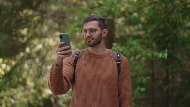 En mannlig turist med en ryggsekk med mobiltelefon i et skogsområde tar en video, fotograferer naturlig utsikt. Utvikling av videoinnhold, direktekoplet kringkasting. – stockvideo
