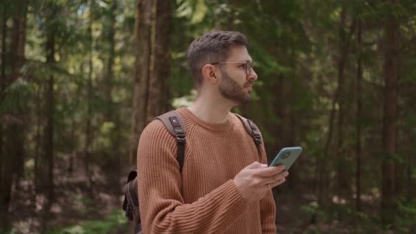 Un viaggiatore di sesso maschile con uno zaino e un telefono cellulare sta camminando attraverso la foresta. GPS, navigatore, mappe online, ricerca posizione. Orientamento sul terreno utilizzando applicazioni sul telefono cellulare. — Video Stock