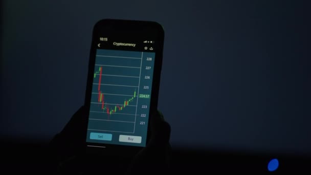 En la pantalla de un teléfono móvil, el gráfico cambia y muestra el crecimiento y la caída de las acciones en el fondo de una tabla cambiante — Vídeo de stock