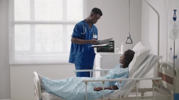 黒人の男性医師が病院病棟の女性患者と話している。治療後の回復はリハビリテーションの開始です。. — ストック動画