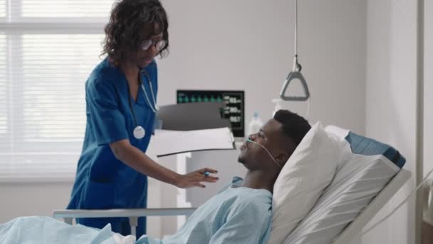 En afroamerikansk kvinnlig läkare kommer till patienten och frågar om hans tillstånd och genomför en undersökning. Diagnos av symtom efter behandling — Stockvideo