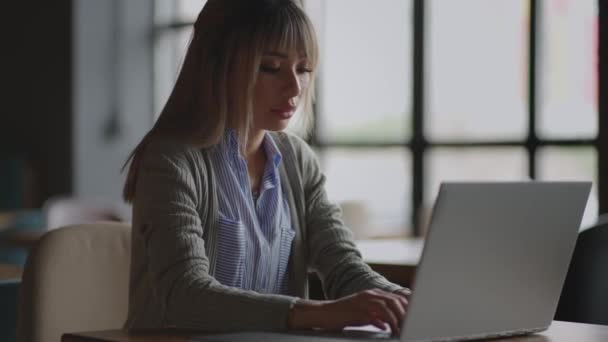 Ung asiatisk attraktiv kvinnlig kontorsarbetare sitter vid den bärbara datorn vid skrivbordet, arbetar och tänker. — Stockvideo