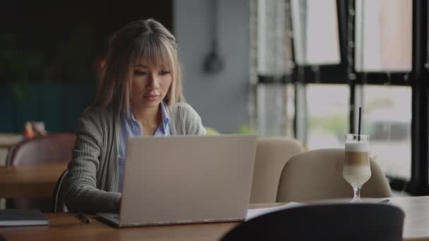 젊은 아시아인 매력적 인 여성 사무직 근로자가 책상에 있는 노트북 컴퓨터 앞에 앉아 일하며 생각하고 있다. — 비디오