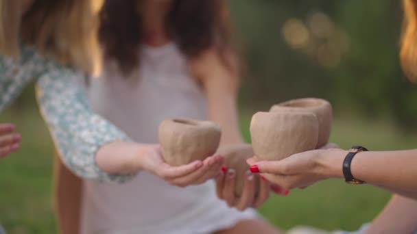 Las jóvenes se dedican al modelado de arcilla en la naturaleza, en el parque, en el espacio abierto. Clases creativas en grupo, formación en modelado de arcilla. Las manos de las mujeres sostienen productos de arcilla en primer plano. — Vídeo de stock