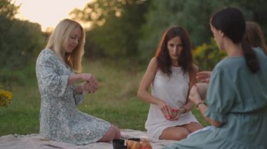 Bir grup genç kadın dikkatle bir çayırda, bir tarlada, bir parkta, açık bir alanda kil yontuyorlar, konuşuyorlar. Yaratıcı aktiviteler, kadın çemberi, iletişim, ortak meşgale.