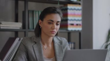 Genç ve güzel bir kadın bir sandalyeye oturuyor ve bir dizüstü bilgisayardaki video ya da ofis toplantısına katılırken not alıyor ya da not alıyor. Modern Müslüman Kadın Giyinen Çalışmalar Çevrimiçi Uzaktan