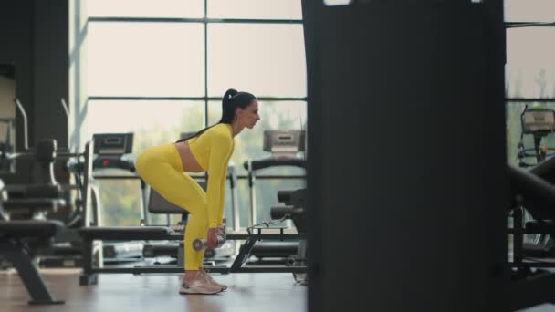 노란색 운동복을 입은 헬스 장에서 만두 벨을 이용해 역도를 하는 체중 감량 여성 . 멍청 한 체구의 여자가 덤벨을 가지고 무리짓기 운동을 하는 모습 — 비디오