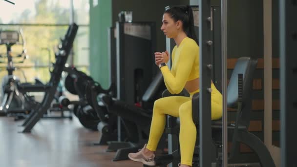 Simülatörde bacak damıtma egzersizi yapan güçlü İspanyol bayan sporcu. Esmer kadın spor salonunda bacak presi yapıyor sarı spor kıyafetleriyle. — Stok video