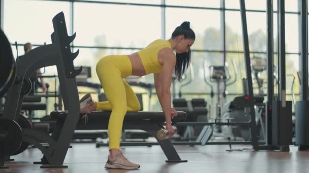 Spor giyim antrenmanındaki İspanyol atlet kadın bir elinde dambılla spor salonundaki tezgaha yaslanıyor. — Stok video