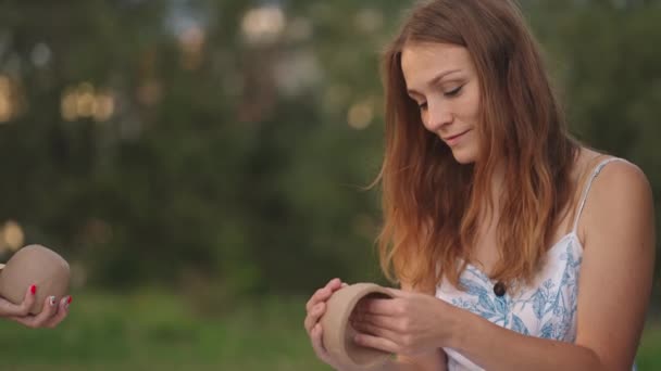 Las mujeres jóvenes forman un producto de arcilla, aplican un patrón, un dibujo sobre productos de arcilla con la ayuda de herramientas, palos en un prado, en la naturaleza, en un espacio abierto. Una mujer esculpe un primer plano. — Vídeos de Stock