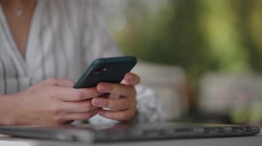 Yazlık bir kafede otururken cep telefonu ekranına yazı yazan bir kadının yakın çekimi. İnternet bankacılığı, mobil sörf siteleri