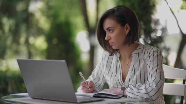 Business Woman Bruneta Arabské hispánské etnika Pracuje na dálku, zatímco sedí v letní kavárně na slunný den s notebookem a píše s perem a notebookem — Stock video