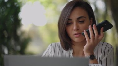 Masanın yanında duran ve dizüstü bilgisayarda yazan akıllı bir telefonda ses tanıma işlevini kullanan çok görevli İspanyol iş kadını. Arap kadın girişimci sesli mesaj gönderiyor.