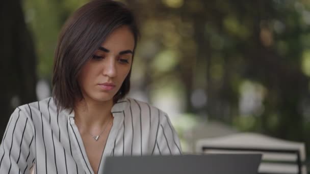 Talentuosa donna seria Bruna Arabo gruppo etnico ispanico siede a un tavolo in un caffè estivo con un computer portatile. Considera la soluzione dei problemi. Donna d'affari confusa. ritratto di una bella donna d'affari — Video Stock