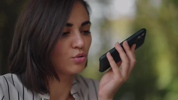 Empresaria hispana multitarea que utiliza la función de reconocimiento de voz en un teléfono inteligente de pie cerca del escritorio y escribiendo en el portátil. Empresaria árabe enviando un mensaje vocal — Vídeos de Stock