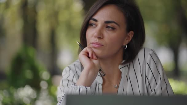 Düşünceli, esmer, Arap kökenli, Latin kökenli bir kadın bir yazlık kafede dizüstü bilgisayarlı bir masada oturuyor. Ciddi iş kadını problem çözme ve iş geliştirme stratejisi üzerine kafa yoruyor — Stok video